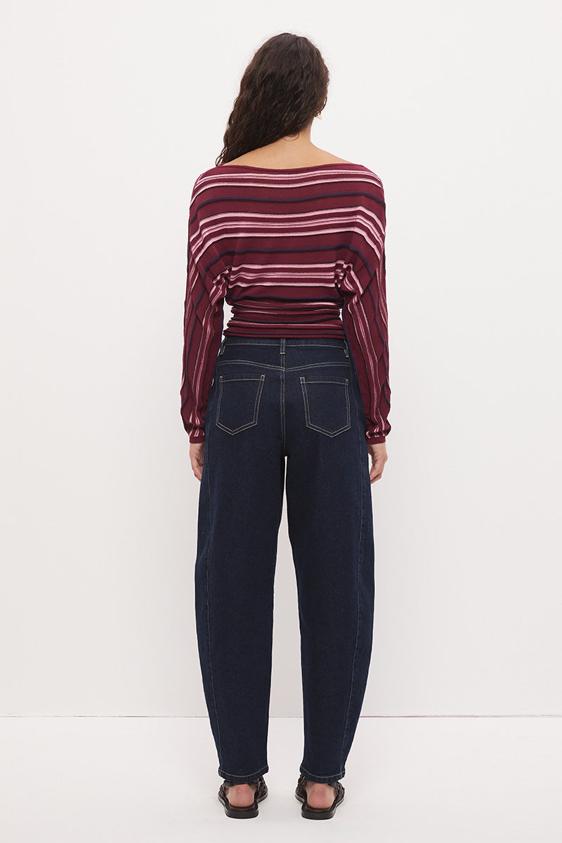 Woman wearing a fully fashioned fine knit long sleeve top in a horizontal multi-stripe with a boat neckline, wide batwing sleeves, dropped shoulders, and soft waistline gathering.
