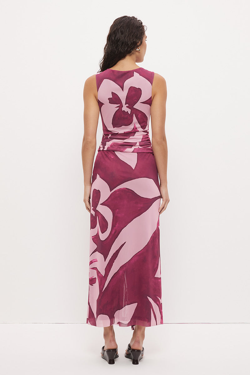Woman wearing a sleeveless maxi dress with an exclusive placement print, sarong-style wrap skirt overlay, ruched asymmetric waistband, and boat neckline in a softly A-lined silhouette